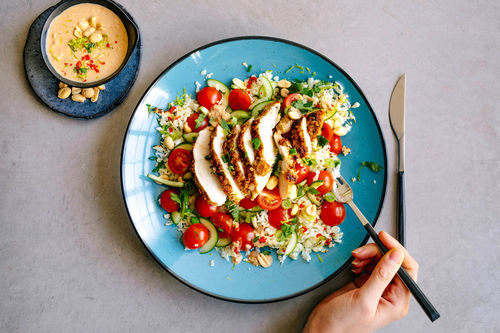 Zarte Satay-Hähnchenbrust auf buntem Blumenkohlreis