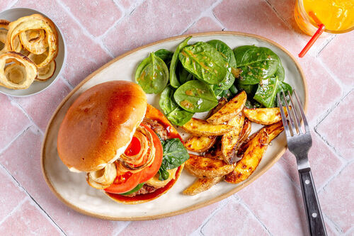 Veganer BBQ-Burger mit Knusperzwiebeln an Kartoffelspalten und Spinatsalat