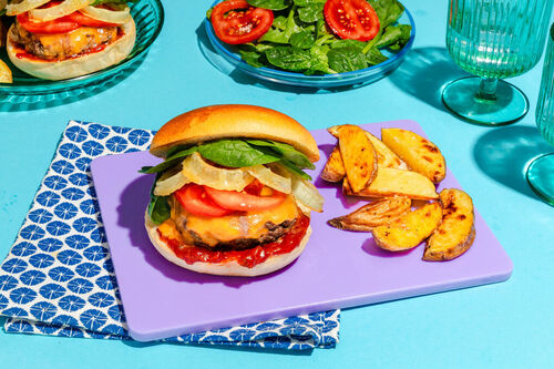 Knuspriger BBQ-Chicken-Burger mit Käse an Kartoffelspalten und Spinatsalat