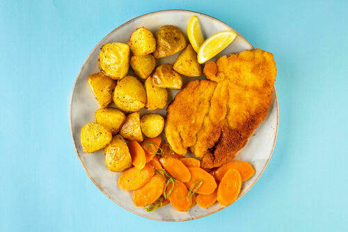 Knusprige Hähnchenschnitzel dazu Röstkartoffeln, Karotten und Zitrone
