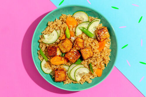 Tofuwürfel auf Teriyaki-Gemüsereis serviert mit eingelegten Gurken