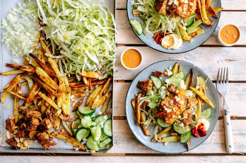 Gebratenes Hähnchen mit Erdnusssauce auf Pommes mit Eisbergsalat und Gurke