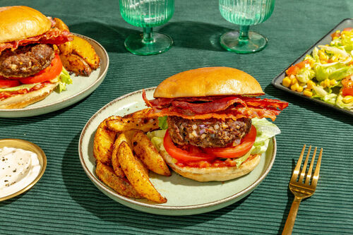 De-luxe-Burger mit Bio-Rind und Bacon dazu Kartoffelwedges und Salat mit Mais