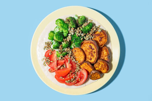 Würziges Röstgemüse auf weißem Bohnenmus dazu frische Tomaten und Sonnenblumenkerne