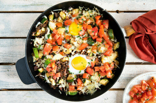 Zucchini-Hack-Pfanne mit Ei und Speck überbacken mit Käse, dazu Tomatensalat